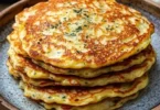 Pancake all'aglio serviti con salsa fresca e decorazione di erbe aromatiche.