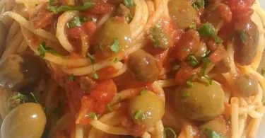 Spaghetti al pomodoro con olive e capperi serviti in un piatto tradizionale