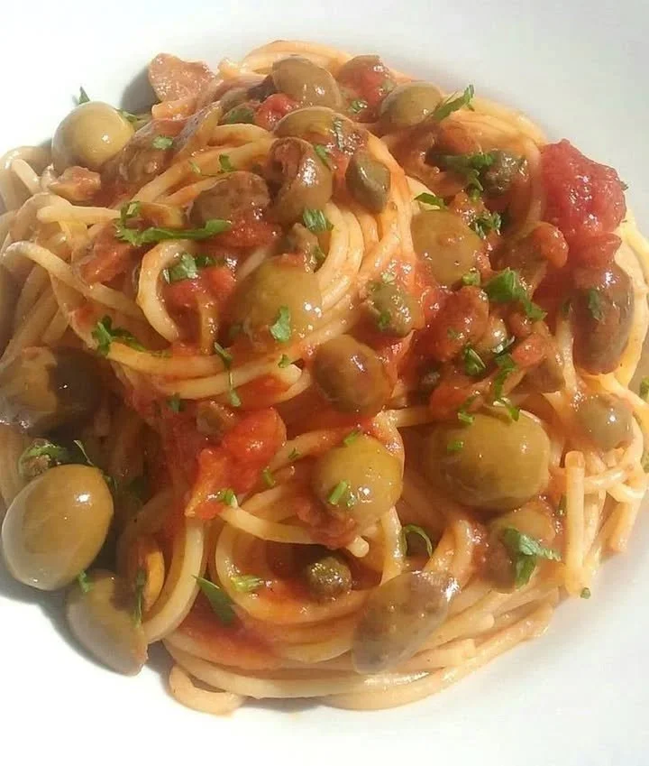 Spaghetti al pomodoro con olive e capperi serviti in un piatto tradizionale