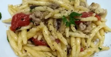 Pasta con salsiccia, funghi e pomodorini servita in un piatto