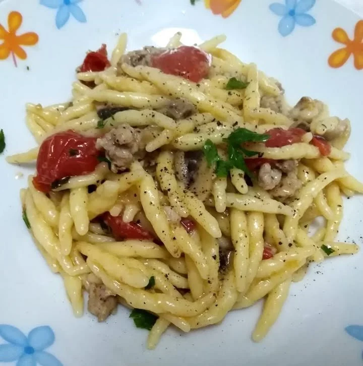 Pasta con salsiccia, funghi e pomodorini servita in un piatto