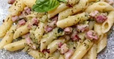 Pasta zucchine e pancetta servita con erbe fresche e formaggio grattugiato
